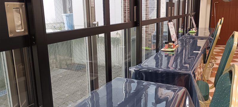 ガラス窓沿いに並ぶテーブル席と緑の椅子