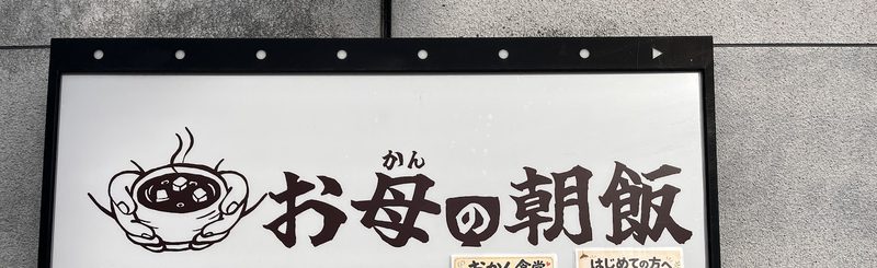 湯気の立つ器のイラストと「お母の朝飯」の文字の看板